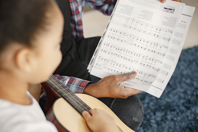 Child playing guitar, learning from music sheets.